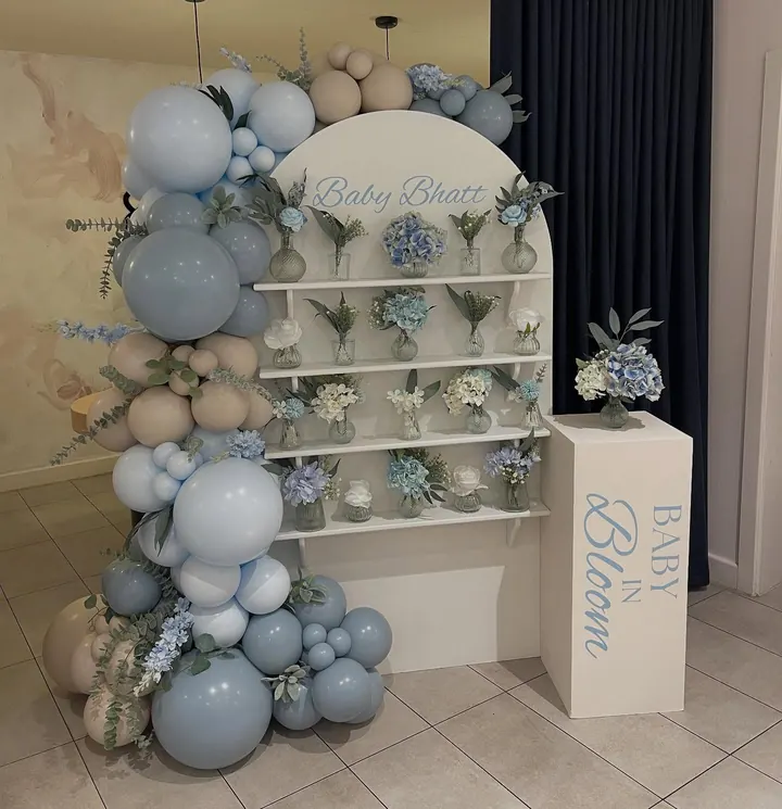 Baby in Bloom backdrop with shelves of flowers in vases, blue and cream balloons and a white plinth