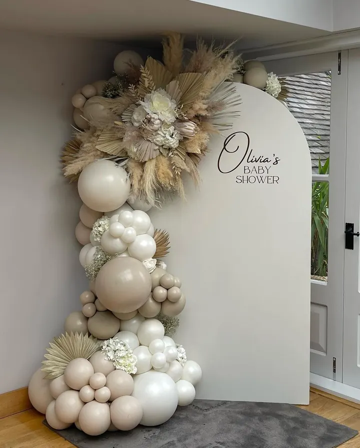 Arch backdrop with a personalised baby shower name, neutral balloons and dried flowers