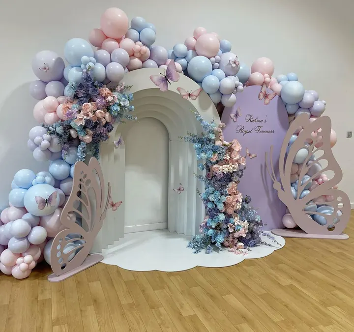 Pastel arch backdrop with butterfly cut-outs, blue and pink balloons and florals