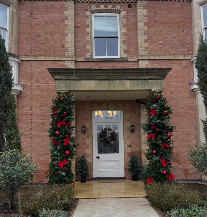 Red and green Christmas garland around the front door of a brick house