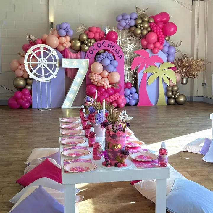 Coachella-themed seventh birthday with a light-up 7, bright pink and purple balloons and a low party table