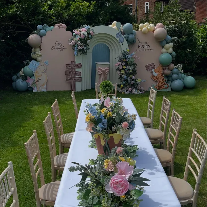 Garden baby shower with a long table, floral centrepieces and a pastel arch backdrop