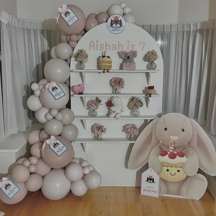 Arch backdrop with shelves of soft toys, blush balloons and a bunny cut-out for a seventh birthday