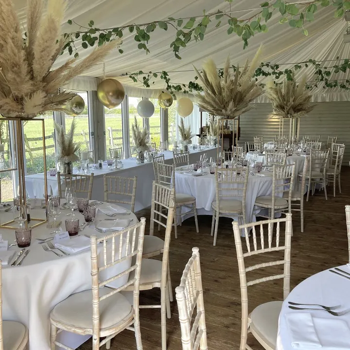 Reception room with white tables, white chairs and tall pampas centrepieces