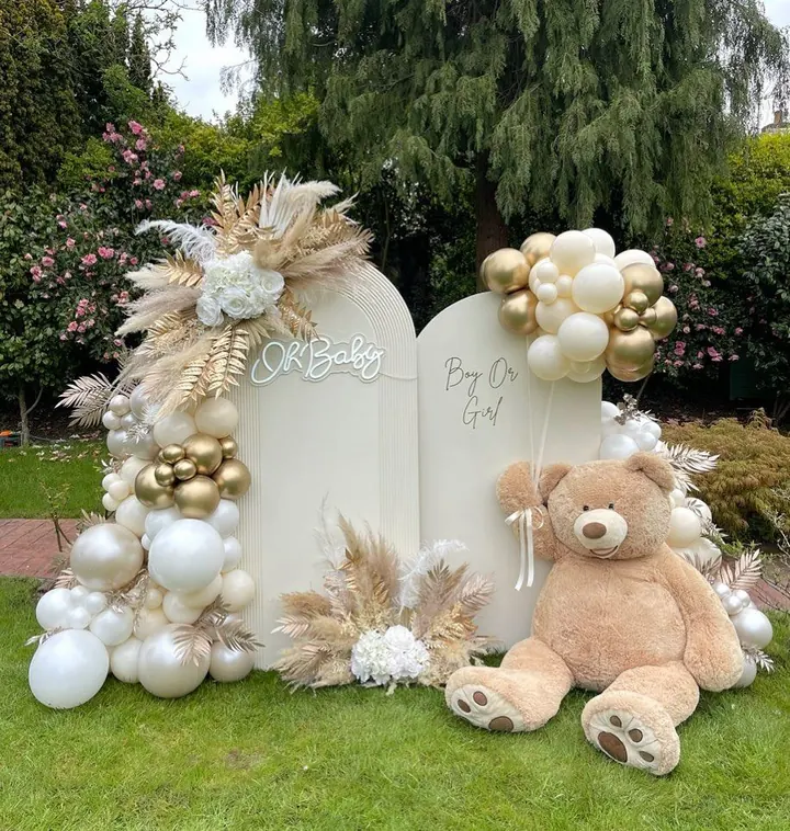 Oh Baby backdrop in a garden with cream and gold balloons, pampas and a large teddy bear
