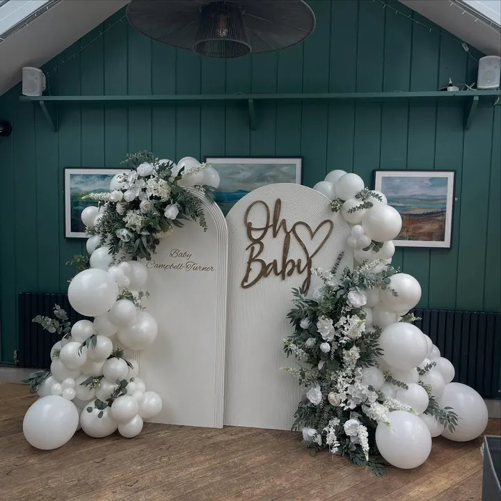 Oh Baby backdrop boards with white florals and white balloons in a green-panelled room