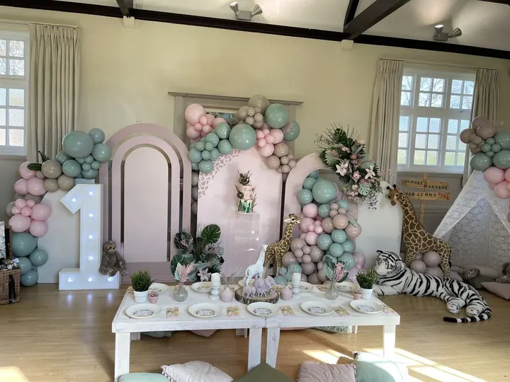 Safari themed first birthday room with pastel balloon garlands, a light-up 1 and animal props