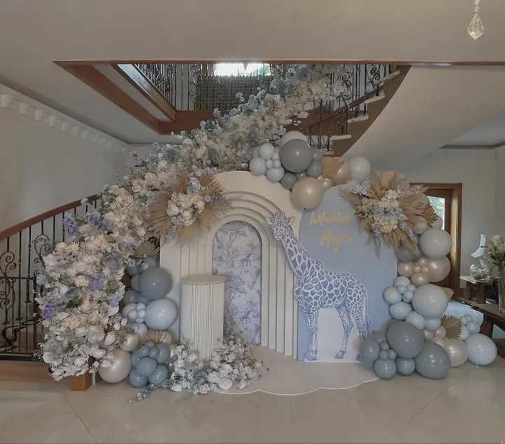 Arch backdrop with a giraffe cut-out, dusty blue and cream balloons and dried florals trailing up a staircase