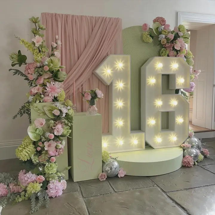 Light-up 16 numbers on a sage plinth with blush drapes, pink faux florals and mirror balls for a sweet sixteen