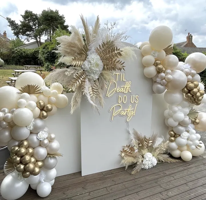 Cream and gold balloon garland with pampas on white backdrop boards reading Til Death Do Us Party