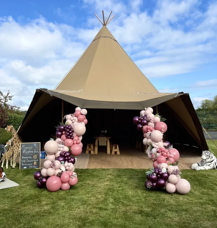 Large tipi tent with pink, burgundy and cream balloon garlands and safari animal props at the entrance